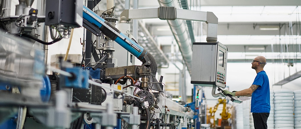 Industrial manufacturing line with a worker operating machinery and overseeing automated production equipment in a factory setting.