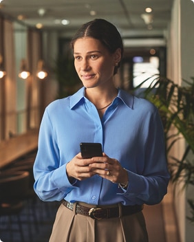 Een persoon staat in een moderne werkruimte en houdt een smartphone vast. Een persoon staat in een moderne werkruimte en houdt een smartphone vast.