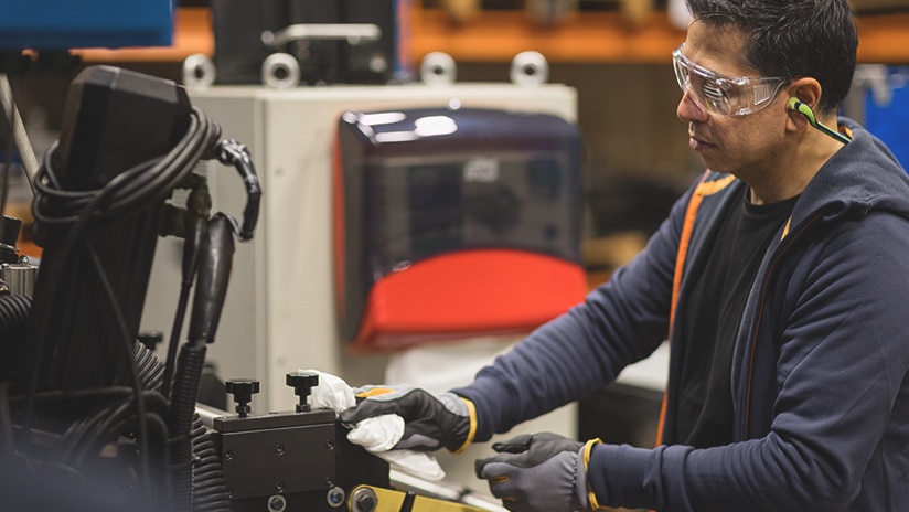 Man wearing goggles wiping a machine with a wiping cloth