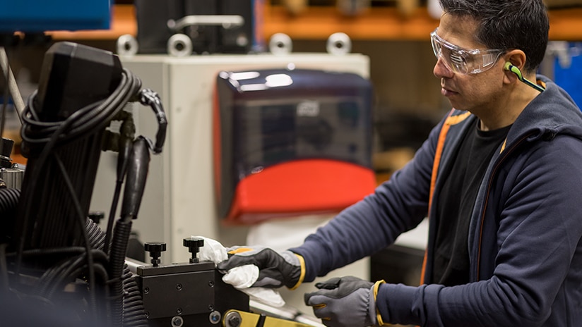 Man wearing goggles wiping a machine with a wiping cloth