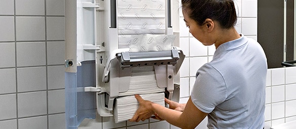 Una limpiadora repone un dispensador Tork con toallas de papel