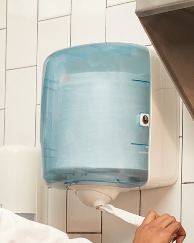 A hand pulling wiping paper from a Tork Reflex dispenser A hand pulling wiping paper from a Tork Reflex dispenser