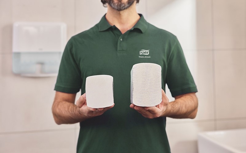 A man in a green piké is hodling two piles with paper towels, the one in the right hand is compressed