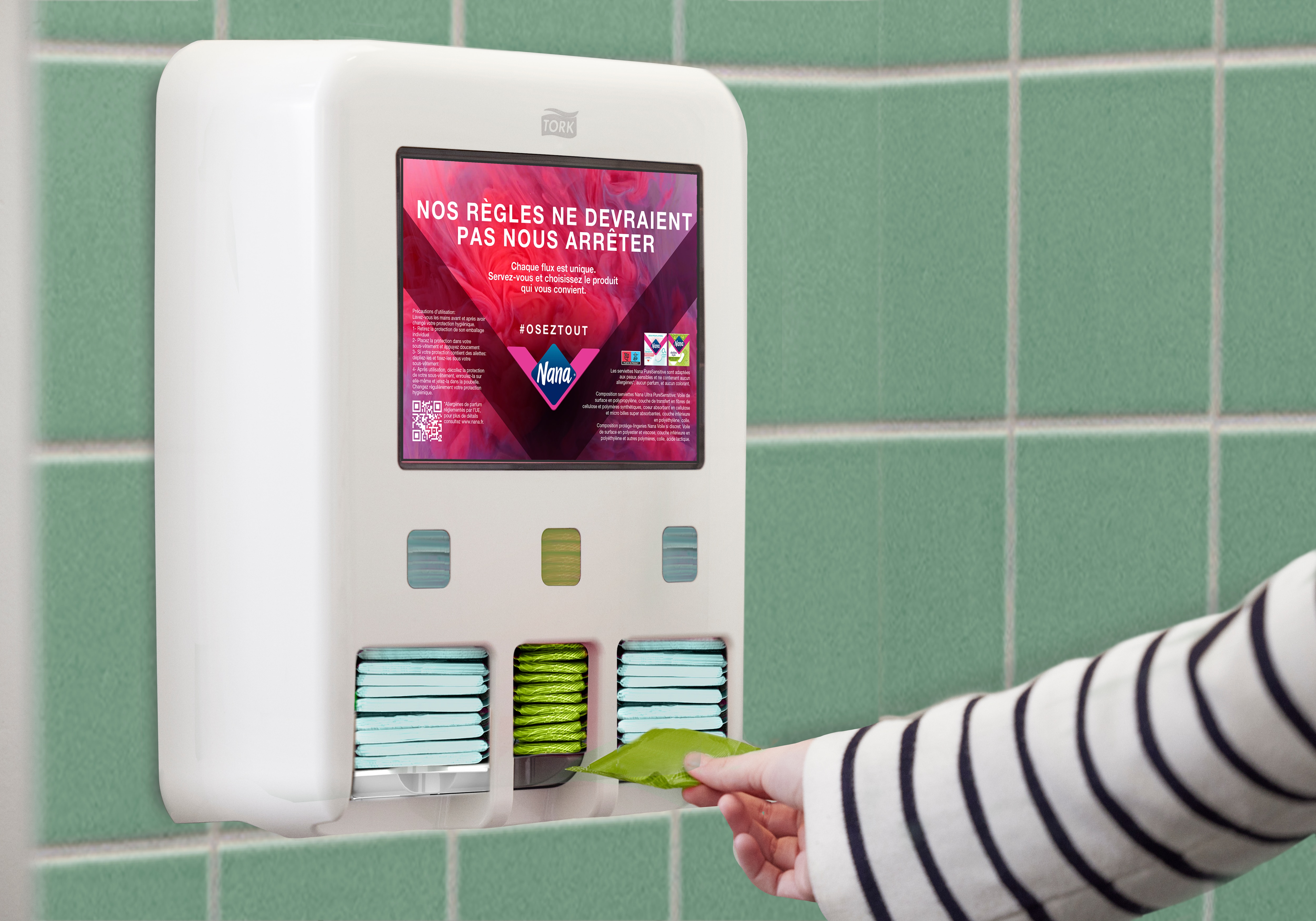 Une personne prend une protection hygiénique d’un distributeur de protections hygiéniques Tork fixé sur un mur carrelé. L’écran du distributeur affiche le message « Le sang ne devrait pas vous freiner ».