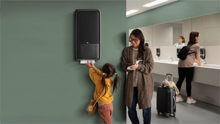 Woman and child in a restroom, child is taking a paper towel from a dispenser