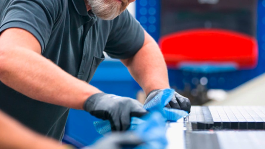 Des ouvriers occupés à polir des équipements sur un site de fabrication; en arrière-plan, un distributeur Tork Performance® rouge cerise pour lingettes/chiffons pliés