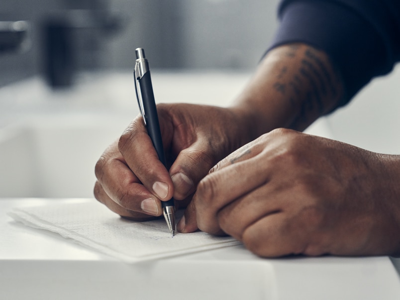 Close-up of a person’s hands writing with a pen on a paper towel in a washroom Close-up of a person’s hands writing with a pen on a paper towel in a washroom