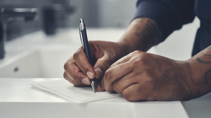 Close-up of a person’s hands writing with a pen on a paper towel in a restroom Close-up of a person’s hands writing with a pen on a paper towel in a restroom