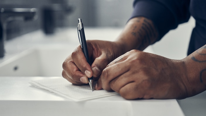 Close-up of a person’s hands writing with a pen on a paper towel in a washroom