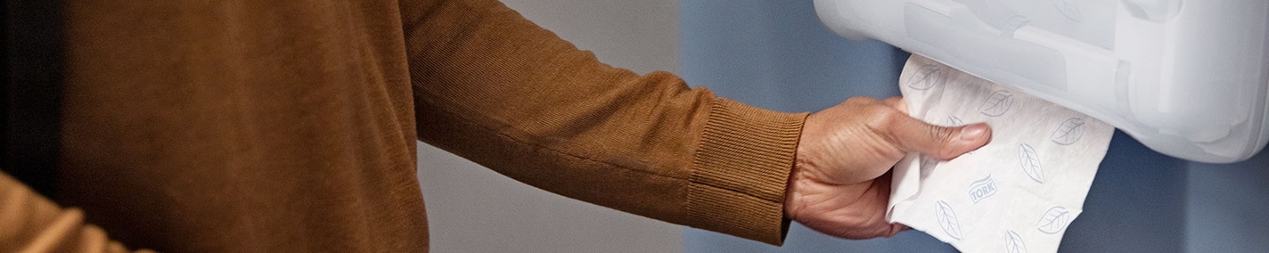 Een persoon die een papieren handdoek uit een dispenser trekt Alt text has not been added