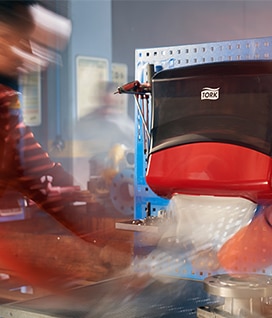 A timelapse image shows one factory worker taking a cloth from a Tork dispenser 