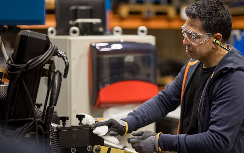 Védőszemüveget viselő férfi ipari munkás papírtörlővel tisztít egy nagyipari berendezést.