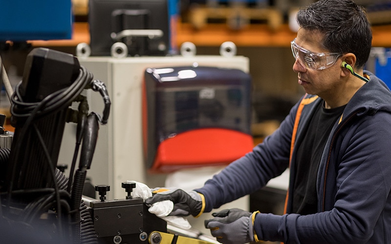 Pracovník v priemysle s bezpečnostnými okuliarmi čistí priemyselný stroj papierovou utierkou.