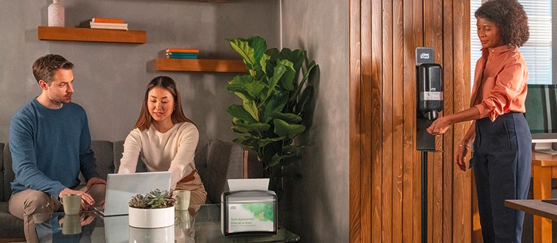 A person using black hand santizer dispenser in office