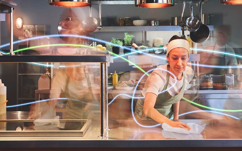 a busy kitchen with a female chef wiping a surface – timelapse