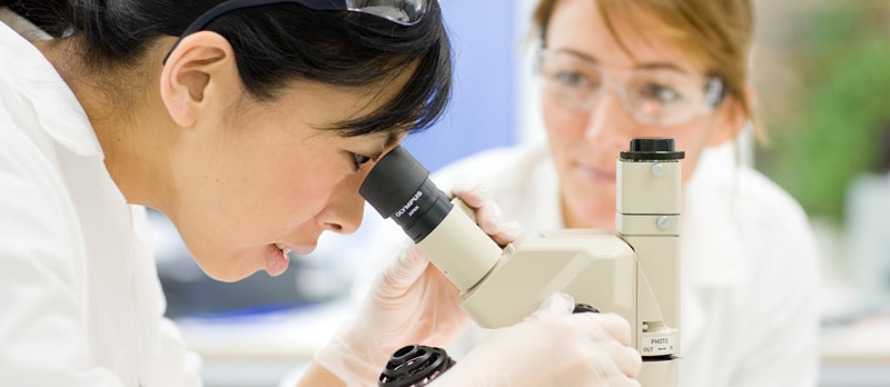 Femme regardant dans un microscope, autre femme en arrière-plan