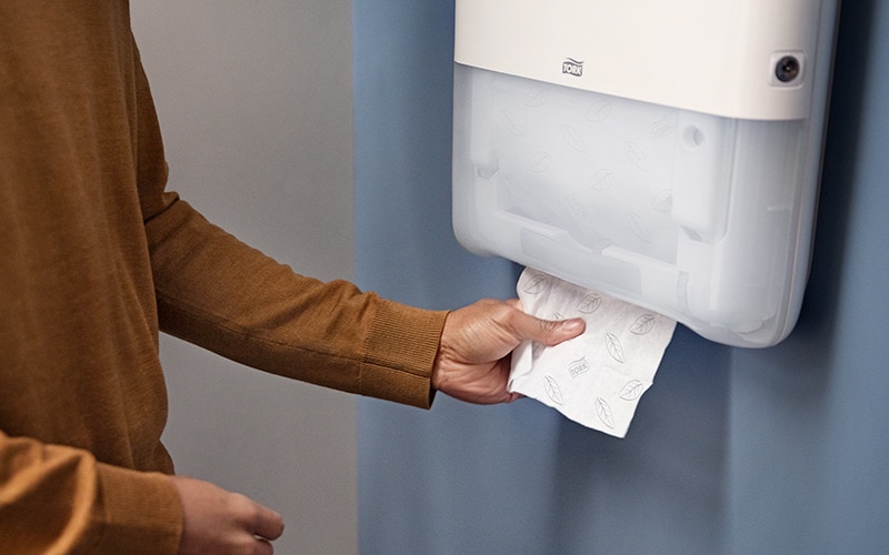 Een hand die een papieren handdoek uit een handdoekdispenser pakt