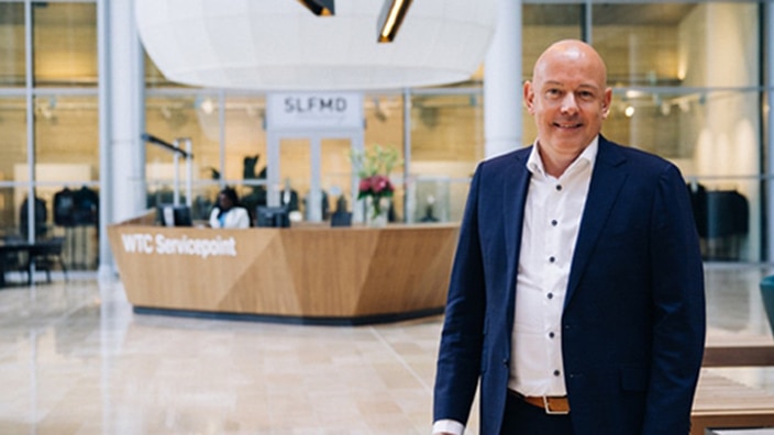 A man standing in a large office lobby looking into the camera