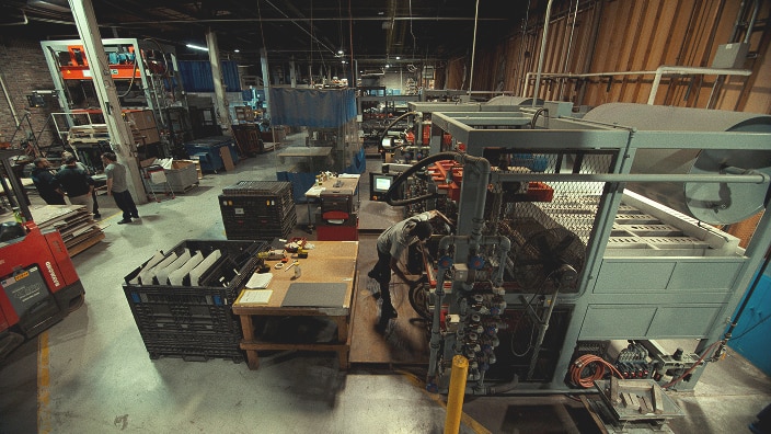 Eine Fertigungshalle mit schweren Maschinen, Arbeitsstationen, Lagerkisten und Mitarbeitenden, die Maschinen bedienen. Eine Fertigungshalle mit schweren Maschinen, Arbeitsstationen, Lagerkisten und Mitarbeitenden, die Maschinen bedienen.