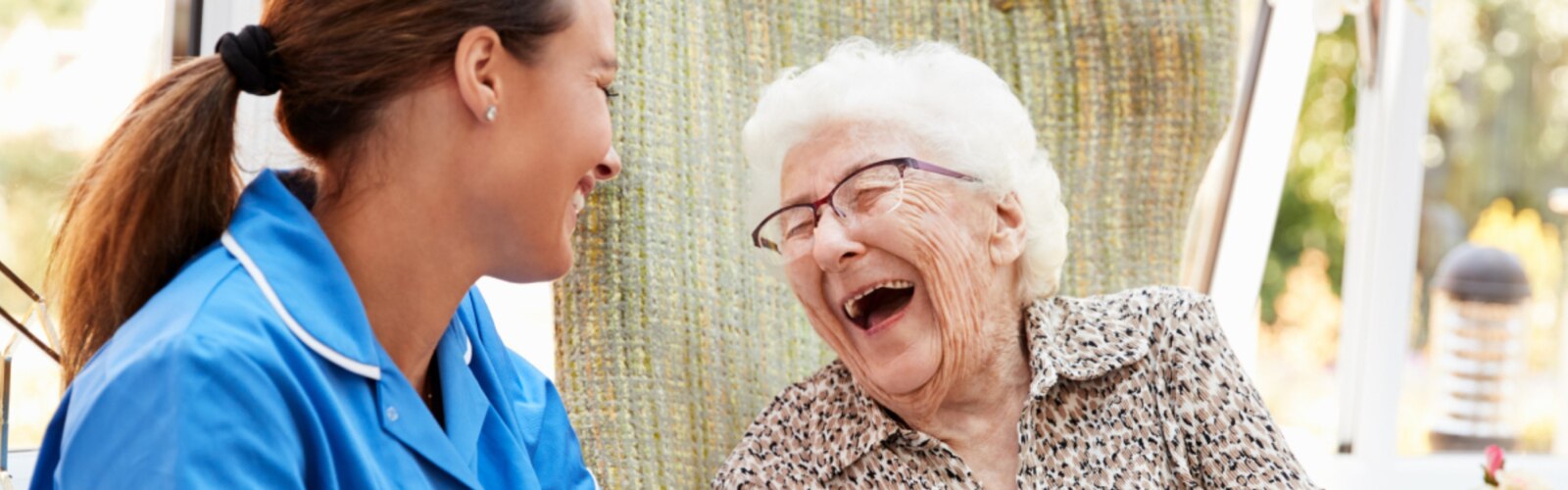 En sygeplejerske og en ældre kvinde griner sammen