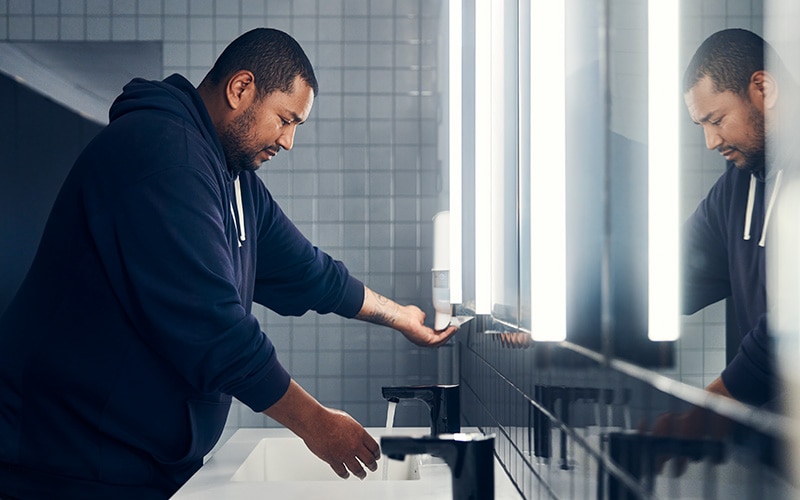 Man in public bathroom using a soap dispenser at a sink