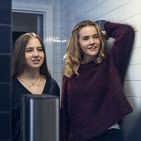 Two teenagers are taking a mirror selfie in a school washroom. Two teenagers are taking a mirror selfie in a school washroom.