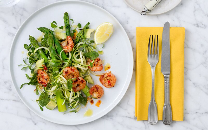 Bord met asperges en vannamei garnalen, bestek en een geel servet 