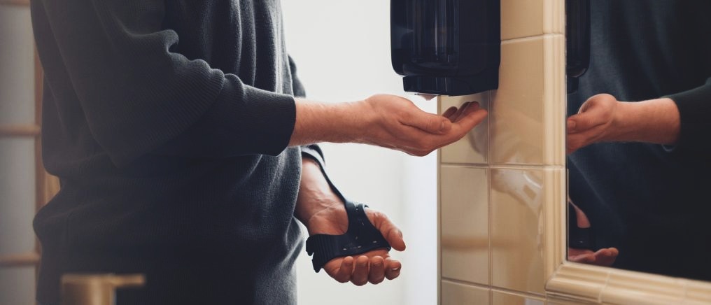 Person använder en väggmonterad dispenser för att få tvål i handen i ett badrum.