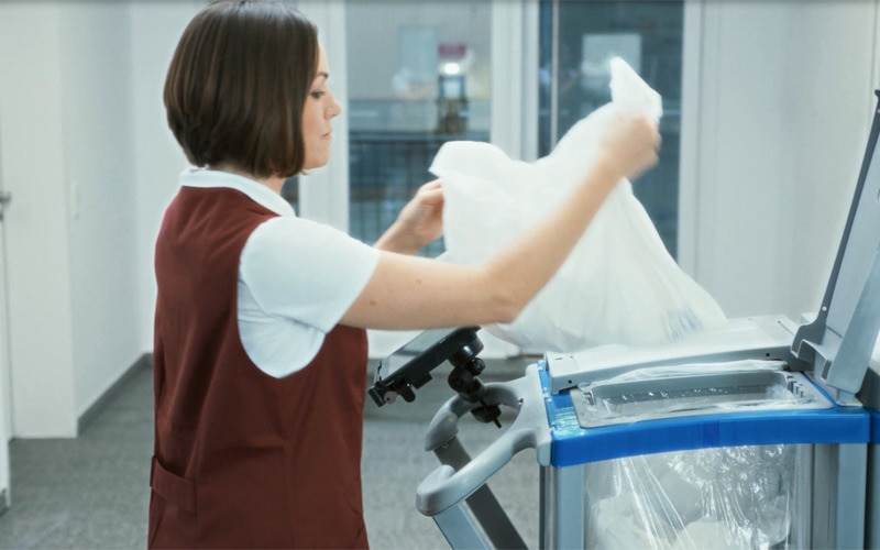 kvinne som kaster papir i en stor avfallsbeholder