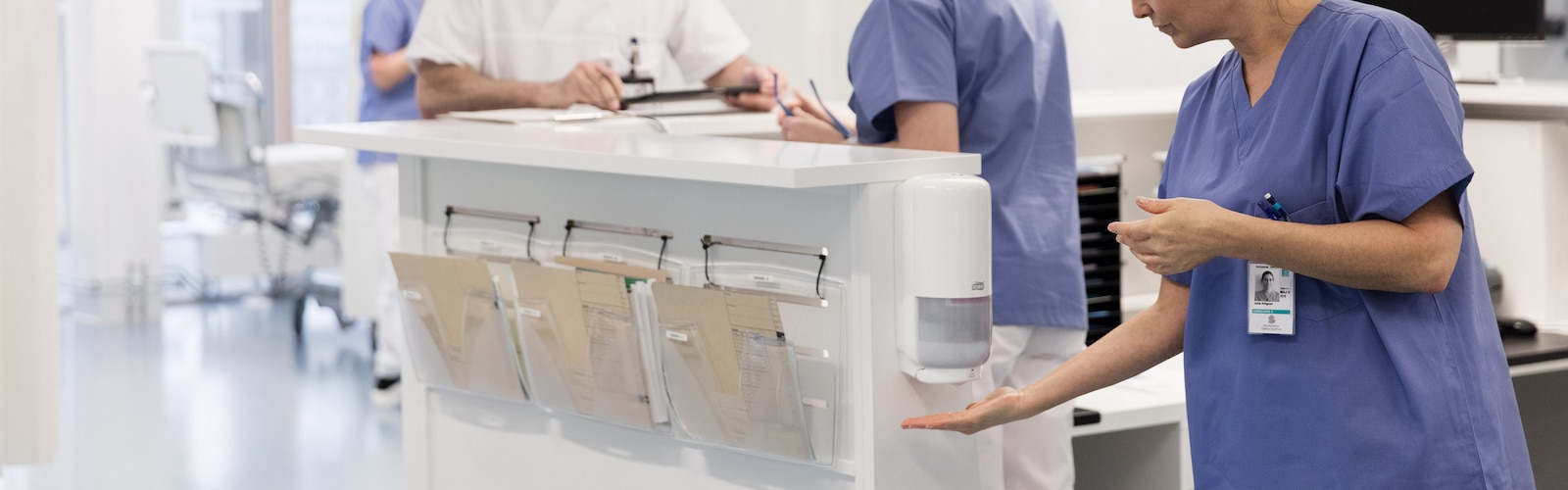 Sjuksköterska som desinficerar händerna via en väggmonterad dispenser