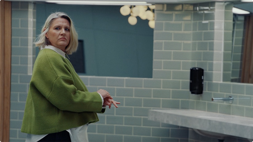 A person in a green jumper smiling and facing a black automatic hand towel dispenser 