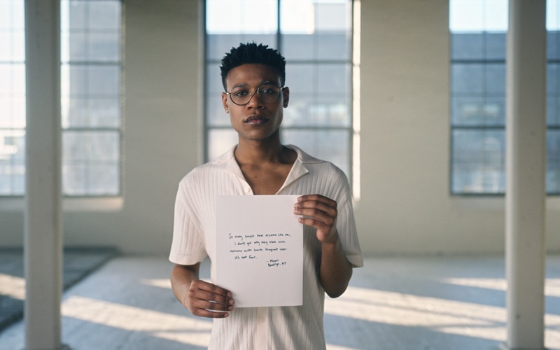 a young man holds a paper towel with handwritten text explaining why fragrant soap can make it hard to use public restrooms
